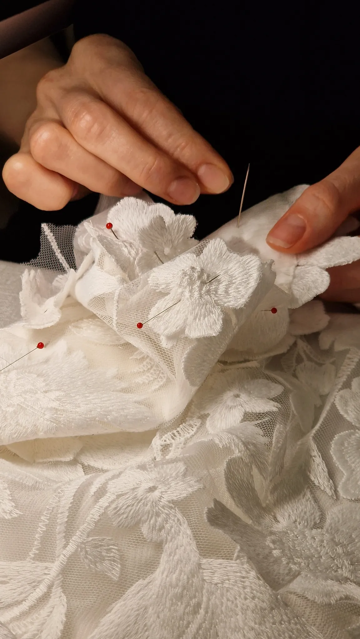 A floral lace appliqué being sewn by hand